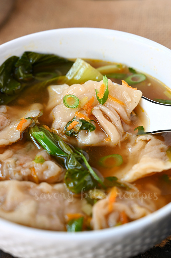 a close up of a white bowl with chicken momos , with bok choy, vegetables in delicious broth