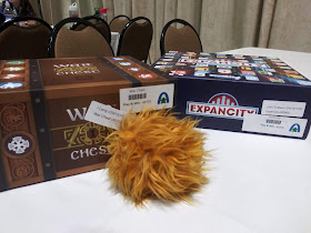 A copy of War Chest and a copy of Expancity, both with stickers on them proclaiming them to be play-to-win prizes and the names of the winners, on a table next to a toy tribble.