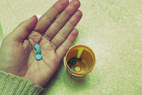 a hand holding several small blue pills. an open pill bottle sits on the counter nearby.