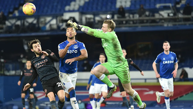 Everton goalkeep Jordan Pickford punches the ball away as City forward Bernardo Silva approaches