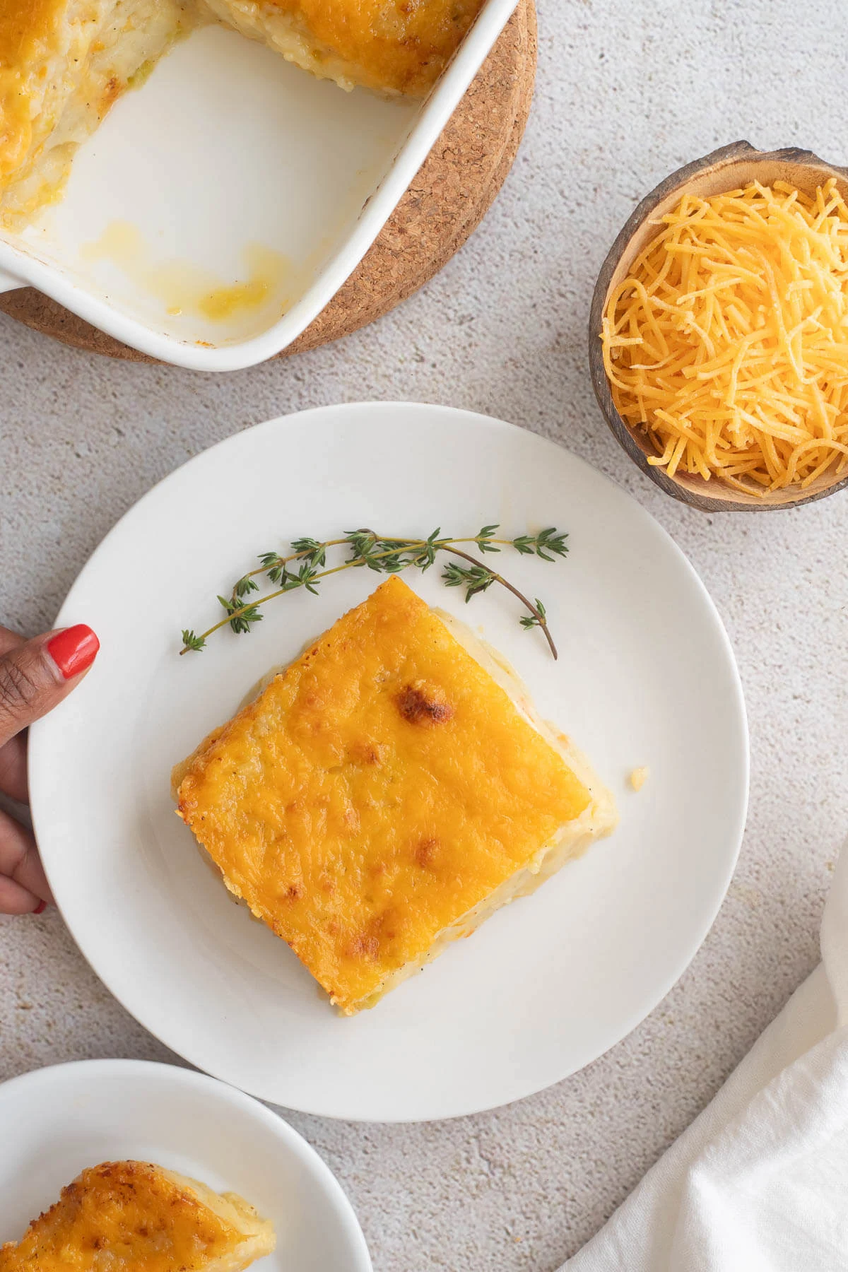 Slice of baked potato pie on a white plate with sprigs of fresh thyme for garnish.