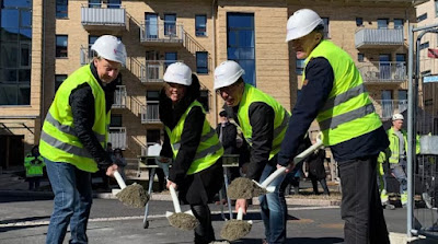 Fyra personer i gula västar och skyddshjälmar tar ett spadtag