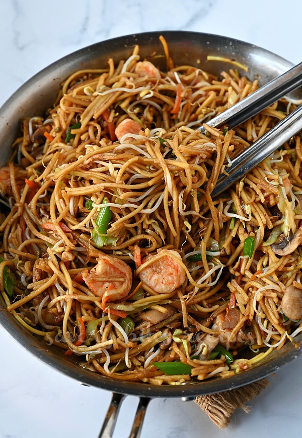 a pair of tongs lifting the shrimp chowmein from the pan