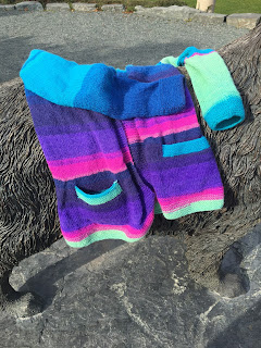 Brightly coloured striped cardigan draped on the back of a Newfoundland dog statue in the sunlight. The cardigan is positioned in a common laying pose as if it were spread on a bed or couch.