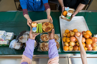 Student Nutrition Services staff hand lunches to students in a cafeteria.