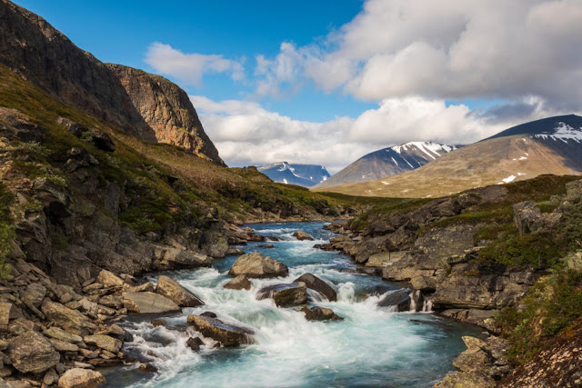 Long Exposure Of A River With Stones In Front Of Mountains While Walking Kungsleden Kings Path Hike In Northern Sweden During Summer