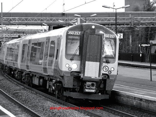 A black and white photo of Class 350257 Desiro EMU train passing at speed through Wolverton station