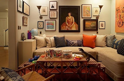 Duża kanapa ozdobiona licznymi kolorowymi poduszkami wcale nie musi być nudna. Dodatkowym ciekawym akcentem wnętrza są obrazy na ścianach i dywan, które razem współgrają.