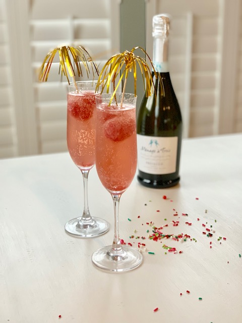 A bottle of champagne and two very pretty cocktails in champagne glasses.