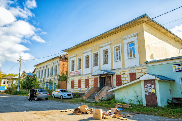 Двухэтажный старый дом и припаркованные машины на широкой улице