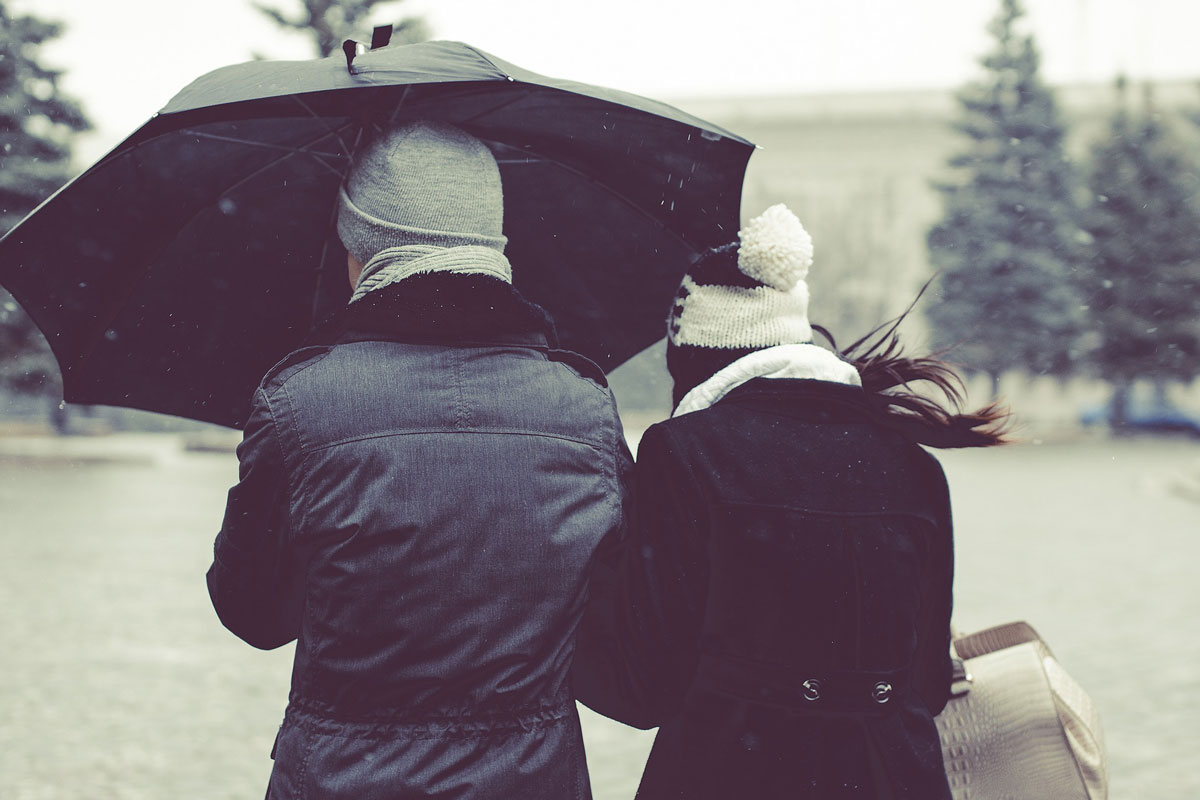 The couple are walking between winter park with black umbrella Featured Image