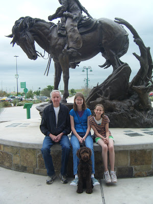 The kids, their Grandpa, and Alfie are seated at the base of an equestrian statue in front of Cabela's.