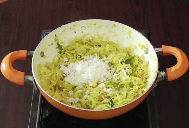 A pan of Cabbage Poriyal with grated coconut being added, the final step in preparation, with the flame turned off.