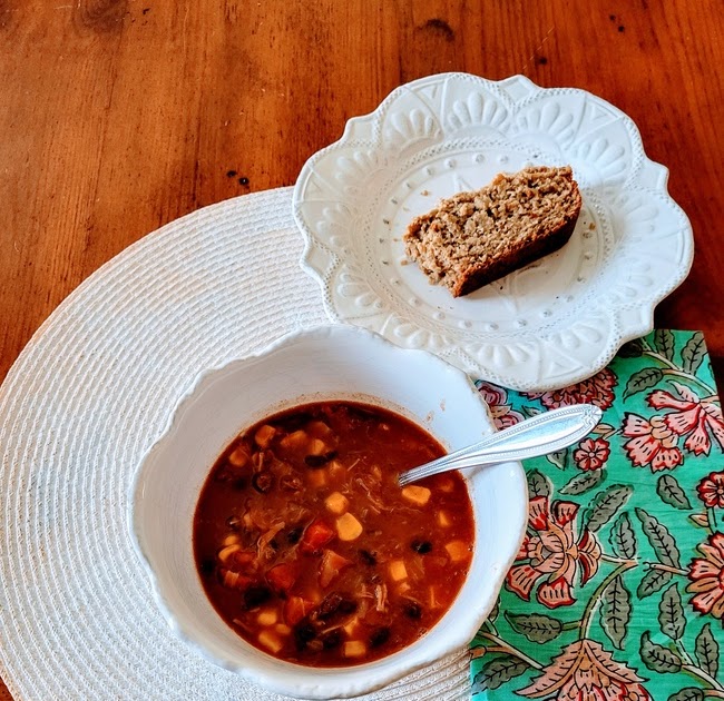 Chili pulled pork served in white scalloped bowl with oat bread side on top of white round placemat