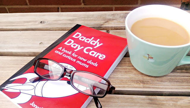 Daddy Day Care book, resting on a bench with a cup of tea and some reading glasses. 