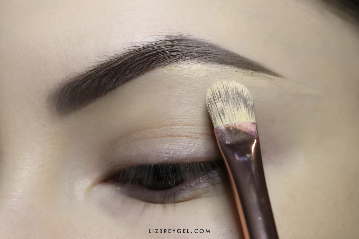 a close-up of woman's brown eye with hooded eyelid  a makeup being applied to the eyebrow