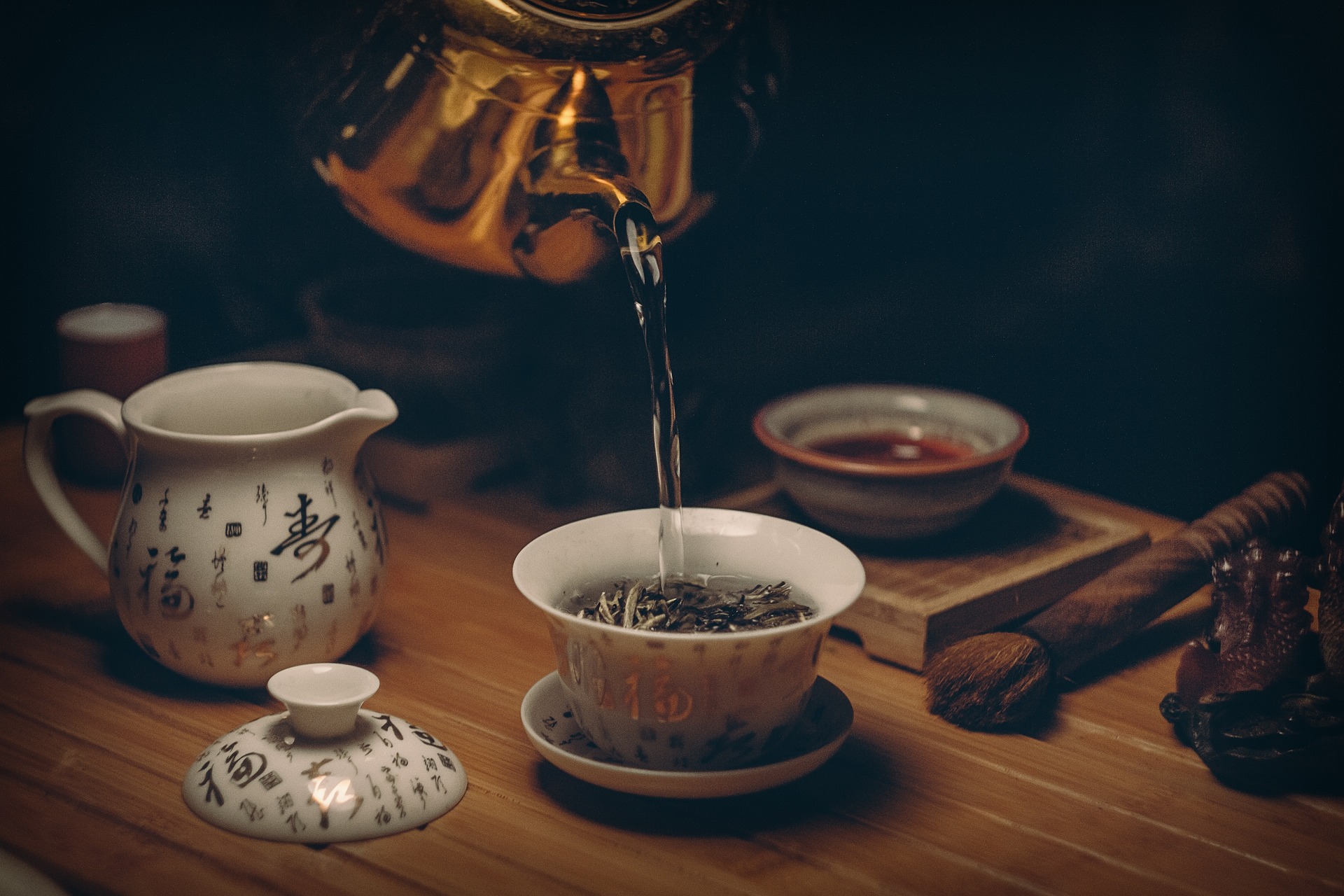 A tea pot is pouring boiling water into a cup with green tea.