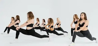 Several women performed leg stretches while wearing black sports bras and black leggings.  Group Aerobic Exercise
