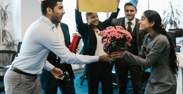 Woman in the office given flowers and greeted by colleagues