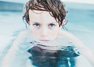 Young boy floating in water up to his chin, looking into camera with blue eyes.