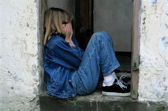 An image of a girl sitting on the window wearing a blue jacket- sad girl dp