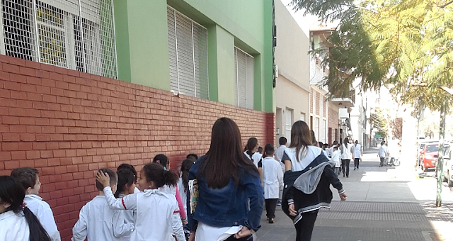 la imagen muestra los alumnos caminando en forma ordenada al lado de la pared de la escuela