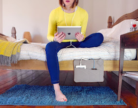 woman sitting on a bed that has a bedside pocket that holds products being charged