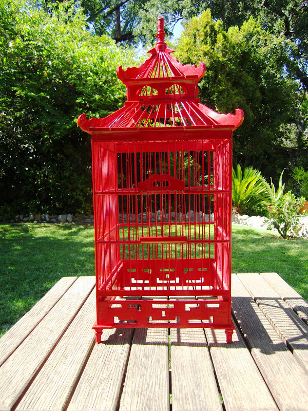 Red chinoiserie style decorative wood bird cage on an outdoor table