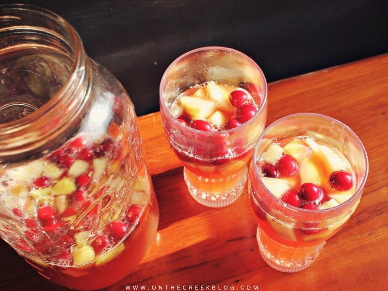 Caramel Apple Punch in a glass pitcher, garnished with fresh-cut apples and cranberries, perfect for fall gatherings. | on the creek blog // www.onthecreekblog.com