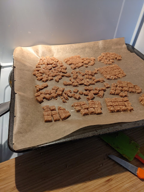 Peanut butter dog biscuits, ready to be baked, on a baking sheet lined with parchment paper. The shapes are small squares.