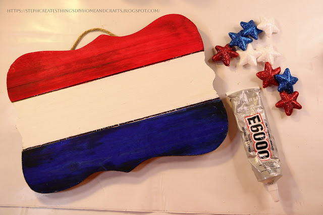 Painted wooden sign with foam stars and adhesive on a table