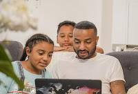 A dad working on his computer with his two daughters peeking over his shoulder