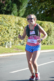Me smiling in the middle of running the marathon with a green hedge behind me.