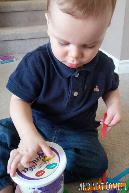 Young toddler putting craft sticks in a container as part of a fine motor color matching activity