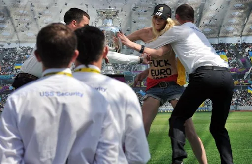 Security tries to stop a female protester as she grabs the European Championship trophy