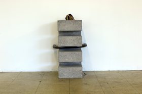 a sculpture on the floor, reaching knee-height, made of  bronze, concrete and steel. Description in text.