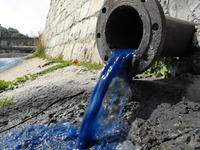 picture of a drain poking out of a dam spilling out blue water.