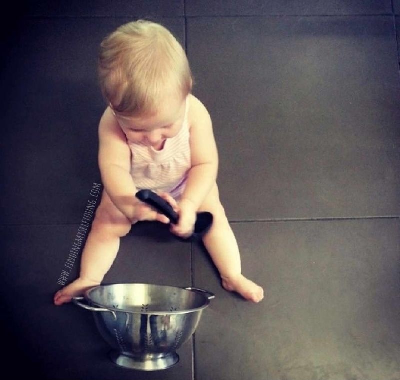 Baby doing heuristic play with a colander and ladel.