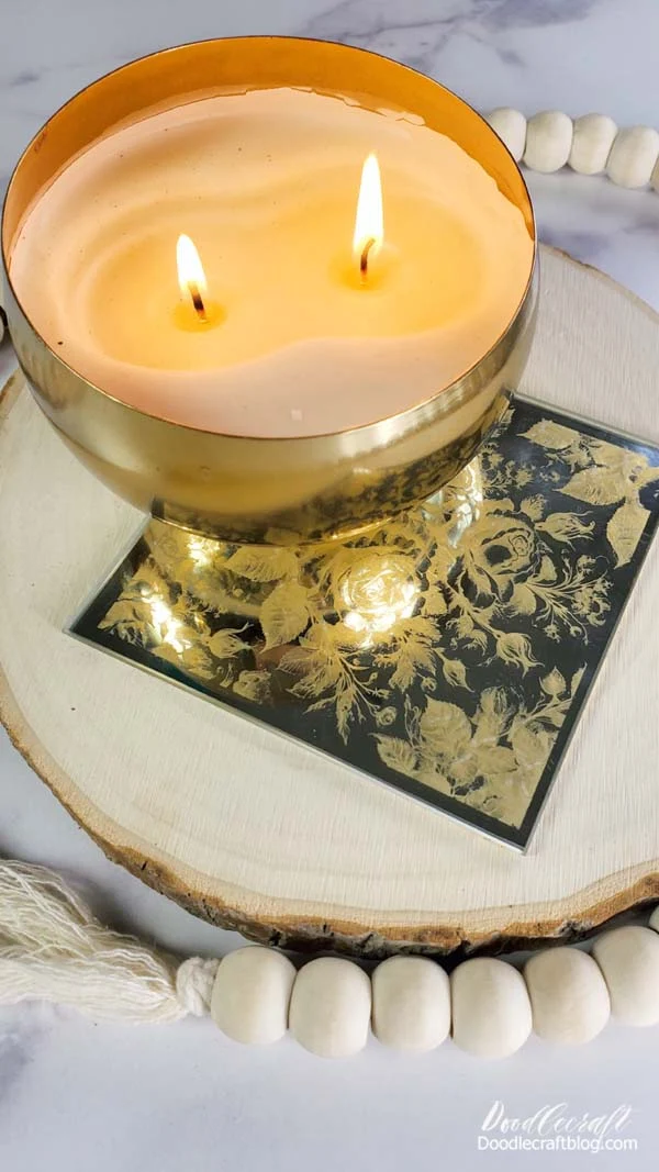 floral engraved mirror with gold leaf backing for a gorgeous two-tone effect sitting on a wood slice and a 2 wick candle in a brass bowl sitting on the mirror.