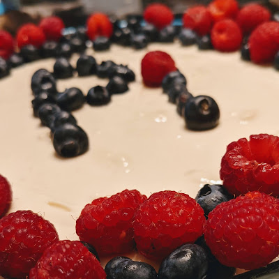 Side view of pie with raspberry close-up and the word "Pi" out of focus in the background