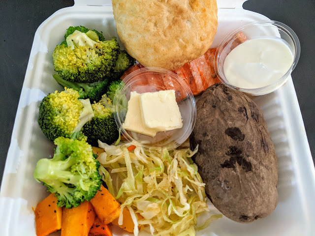 Container full of vegetables (brocolli and sweet potato), coleslaw, baked potato, butter, sour cream, salmon, and Bannock