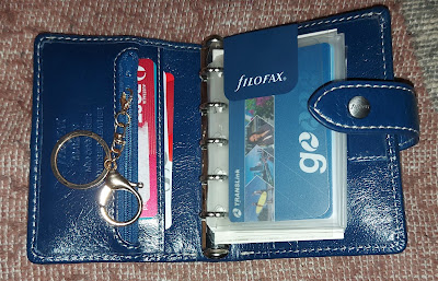 open Filofax navy blue mini ring bound organiser, with a rose gold key chain on the zip that is on left hand side, and travel and credit cards visible in the pockets and card sleeves