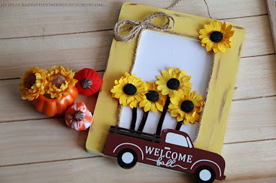 Painted yellow picture frame with yellow paper sunflowers and red truck decoration displayed by mini pumpkins