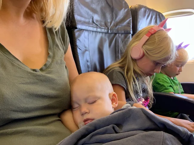 3 children and mum on an aeroplane. The baby is asleep and children on iPads