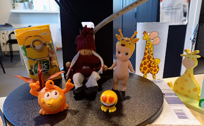 Angel tussen een doosje van Miniontiktaks, een oranje beestje, een winterpoppetje, staande smiley met hartoogjes, gevouwen kraanvogel, giraffeglas en giraffe pennenbeker