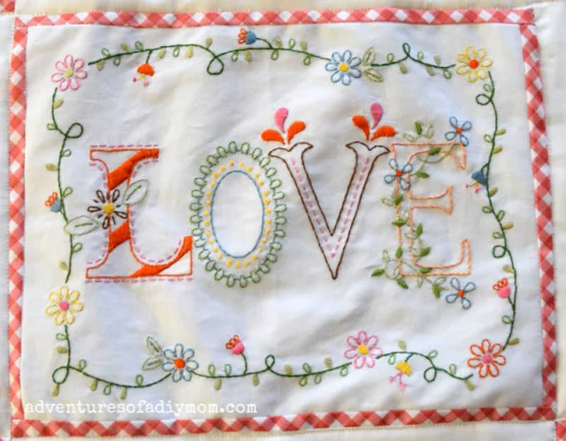 an embroidered piece of fabric with the word love and bordered with flowers