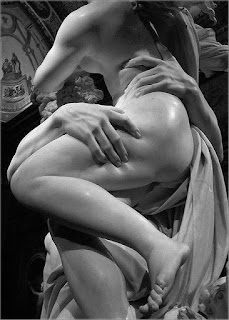 Foto em preto-e-branco de parte de uma escultura em mármore de Bernini. Proserpina, nua, apoiada em Hades que a sustenta acima dos ombros. A mão direita de Hades apalpa fortemente a coxa de Proserpina que está com o corpo de perfil à esquerda, perna esquerda levemente sobre a outra fazendo sombra sobre o joelho direito; o delicado pé esquerdo, posicionado para baixo está no ar; a outra mão de Hades apalpa a cintura e o dedo indicador afunda sobre a carne. No topo, parte das pontas dos cachos dos cabelos ao vento, nas costas, uma sombra contrasta o brilho de um foco de luz sobre o ombro e parte do braço em ângulo a frente do corpo deixando a mostra o delineio de parte do seio esquerdo próximo aos cabelos ondulados de Hades. Entre os dois, um manto com dobras, pregas e ondulações. No teto, uma pintura com duas figuras humanas.