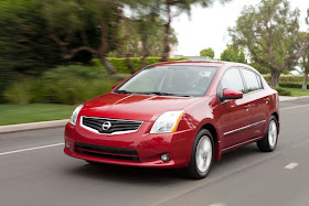 Front 3/4 view of red 2011 Nissan Sentra sedan driving on suburban street