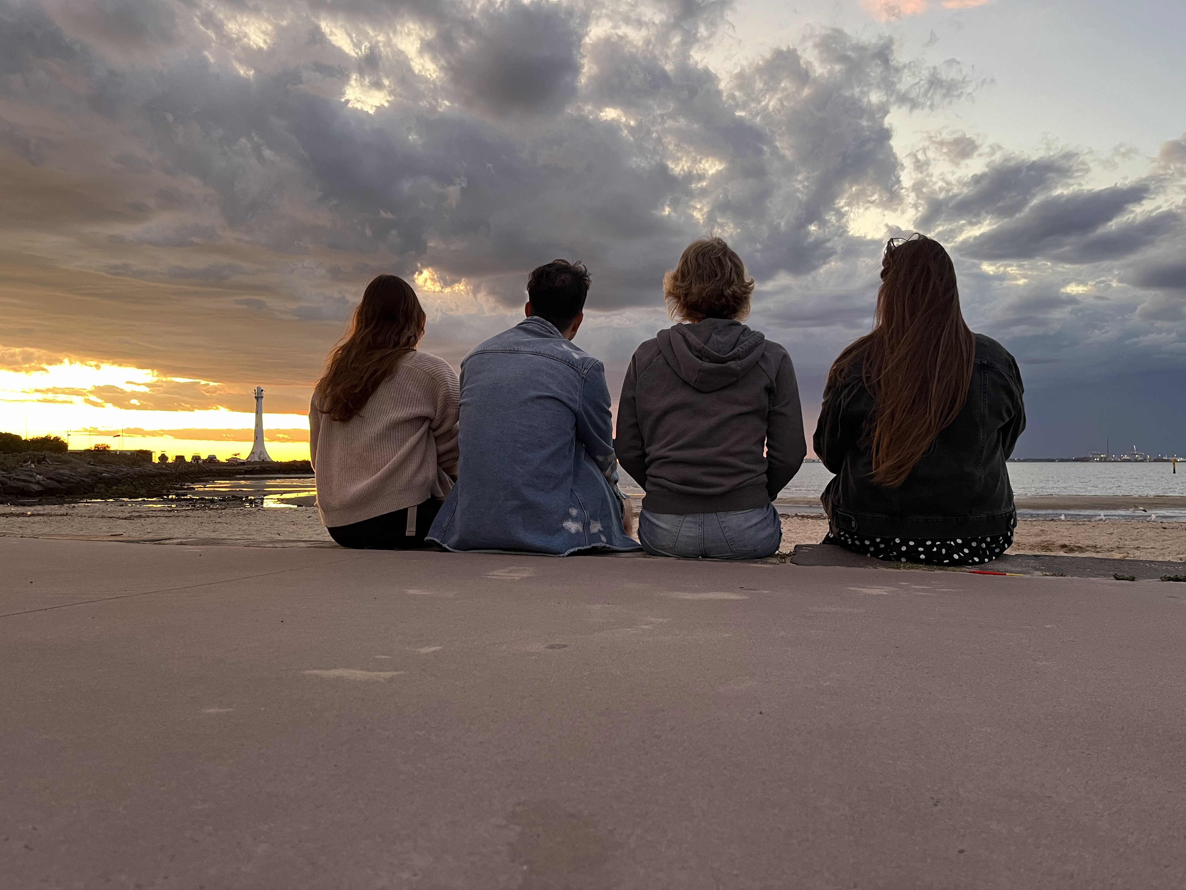 Four friends sitting with their back to the camera, they are watching the sunset across the bay.