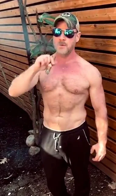 Sunglasses wearing shirtless sexy muscular man blowing out cigar smoke